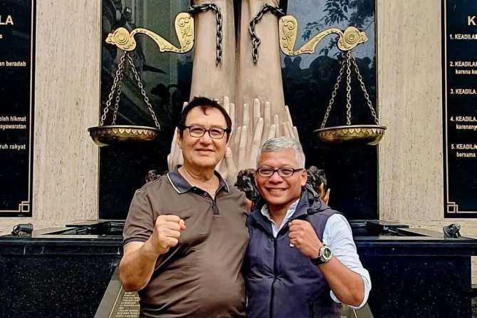 Two men posing together at an outdoor monument during an electric field therapy forum in Medan